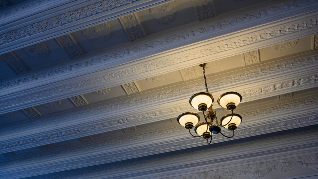 Elegant decorative false ceiling with ornate moldings, coffered ceiling panels, and classic chandelier lighting in a luxury interior space.