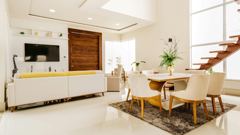 A sophisticated modern interior featuring a cream sofa, sleek dining set, and floating staircase bathed in sunlight — blending minimalism with luxury warmth.