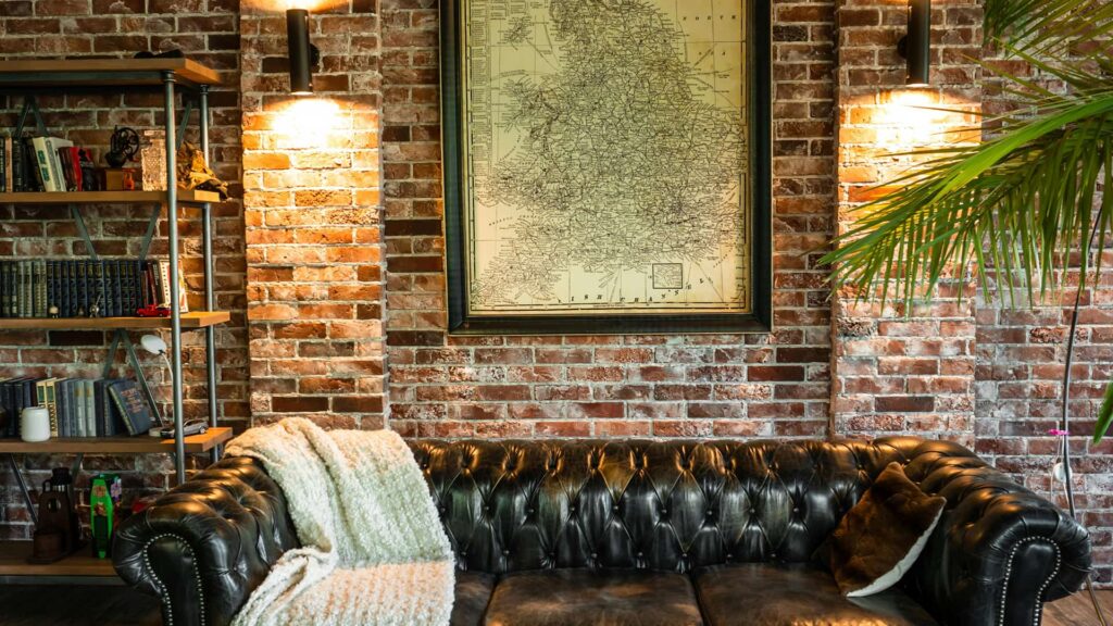 A refined reading nook with a tufted leather couch, England map artwork, and ambient wall lighting against exposed brick — evoking timeless British charm and comfort.