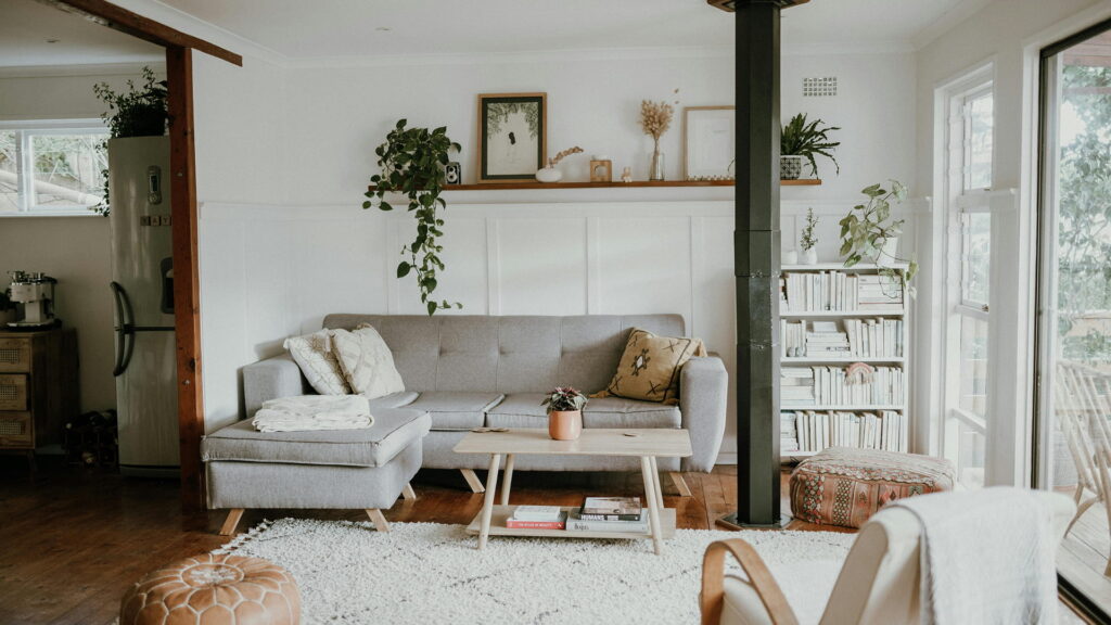  A serene, light-filled space with a gray sectional sofa, wooden accents, and lush indoor plants — exuding cozy, organic charm.