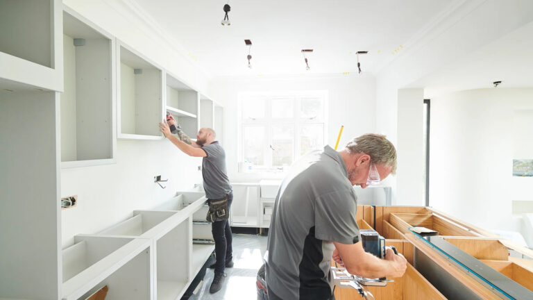 Interior renovation workers installing custom kitchen cabinets and fittings in a bright modern home.